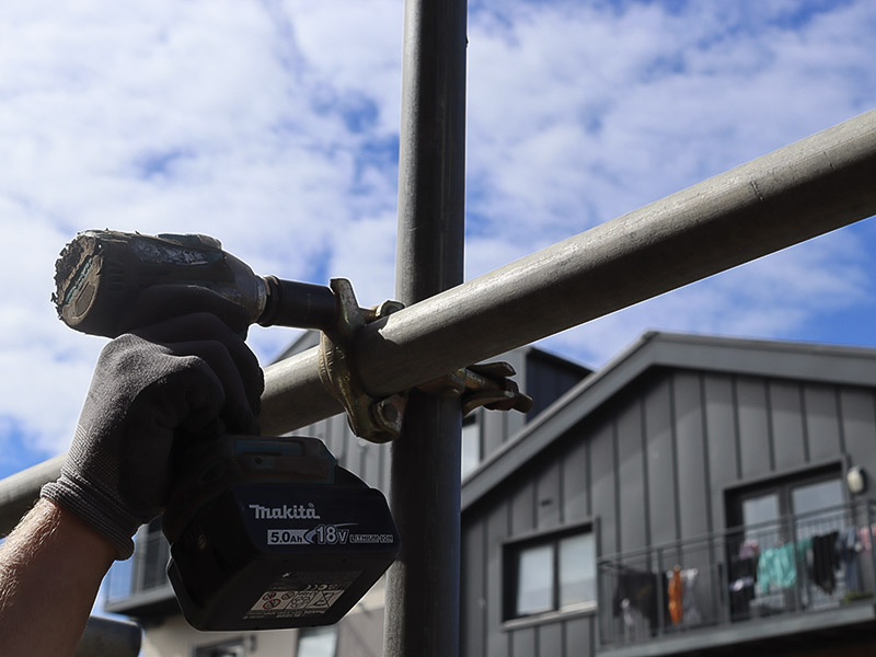 A gloved hand tightening a scaffold fitting with an impact driver